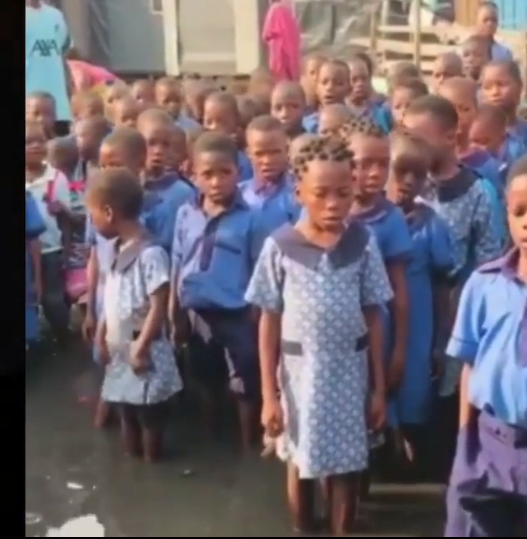 Outrage as school pupils are seen singing the national anthem inside dirty water, govt reacts (video)
